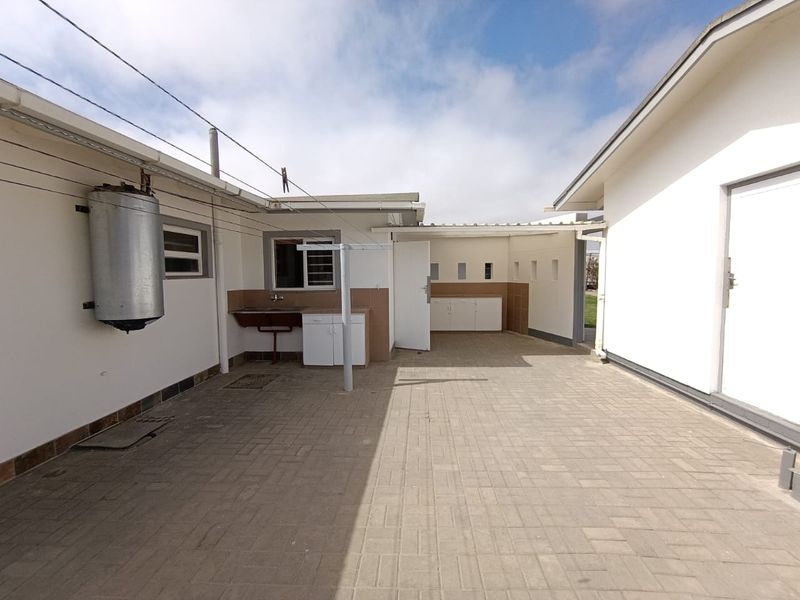 A functional outdoor utility area featuring a paved courtyard, external geyser, and built-in sink with storage cabinetry.