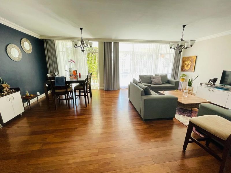 Spacious open-plan living and dining area featuring warm hardwood flooring, large sliding glass doors for natural light, and elegant ceiling cornices.