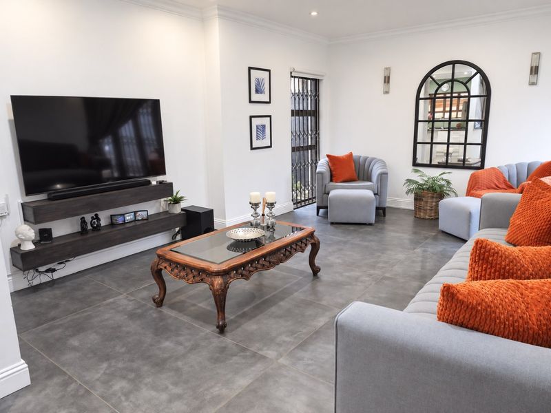 A modern, well-maintained living room featuring large format floor tiles, a floating media console, and elegant coving with recessed lighting.