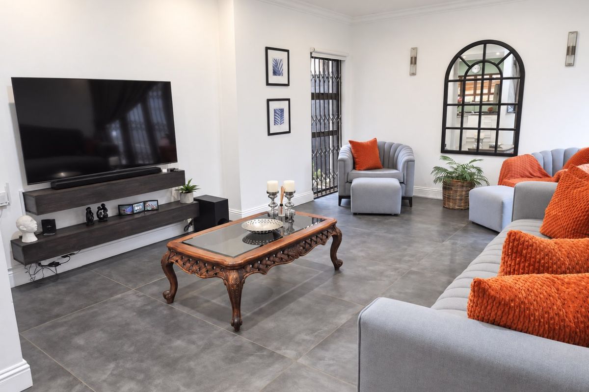 A modern, well-maintained living room featuring large format floor tiles, a floating media console, and elegant coving with recessed lighting.