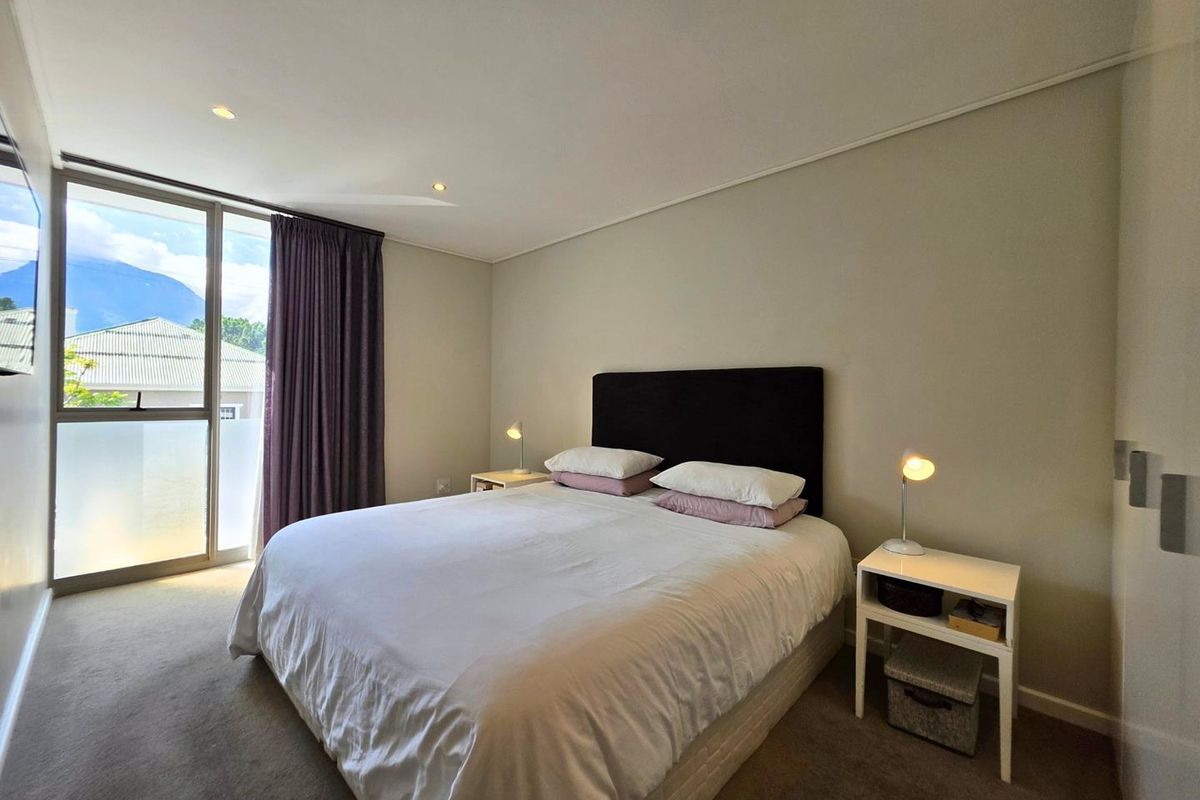 A well-maintained bedroom featuring neutral carpeting, recessed ceiling lighting, and a large sliding glass door providing natural light and access to a balcony.