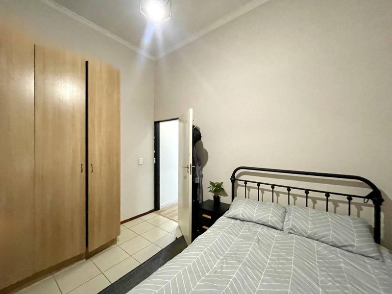 A functional bedroom featuring tiled flooring, a built-in wardrobe, and neutral wall finishes, providing a clean and practical living space.
