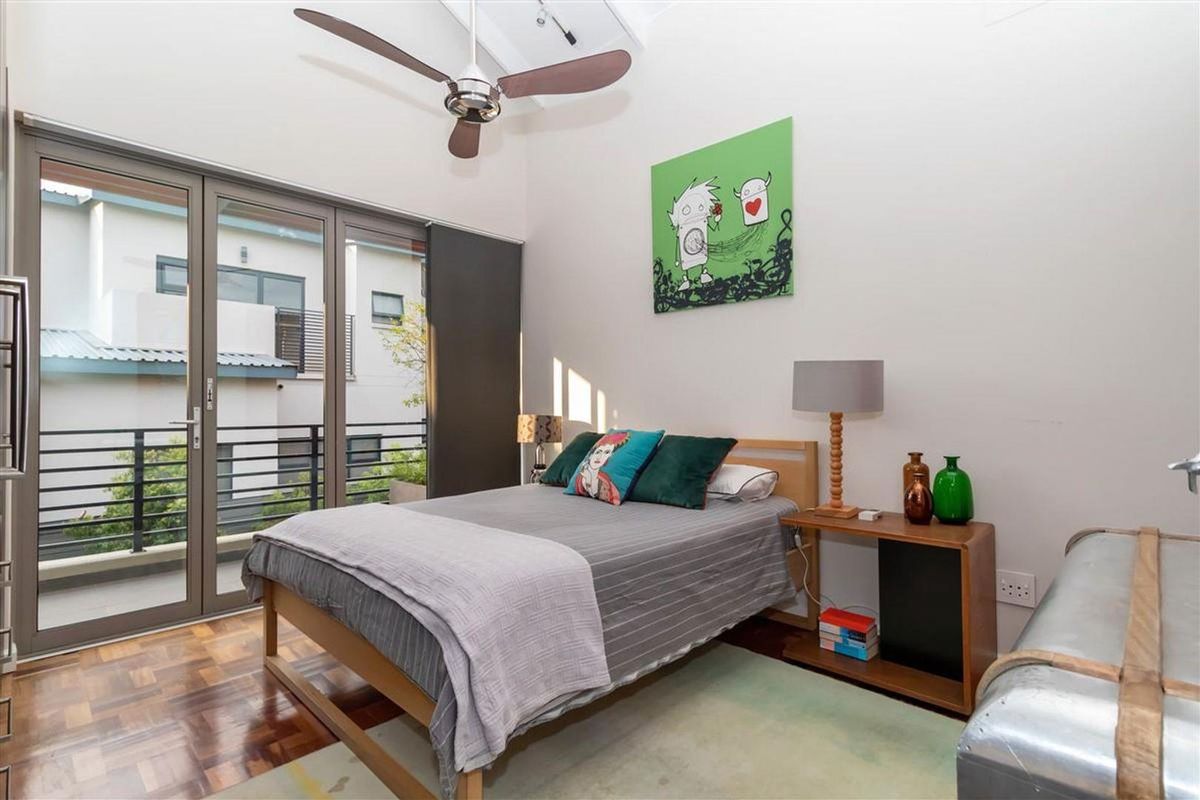 A bright bedroom featuring high vaulted ceilings, a ceiling fan, and large sliding glass doors that open onto a private balcony.