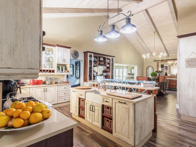 Spacious open-plan kitchen and dining area featuring a farmhouse sink, kitchen island, vaulted ceilings with exposed beams, and high-quality cabinetry.