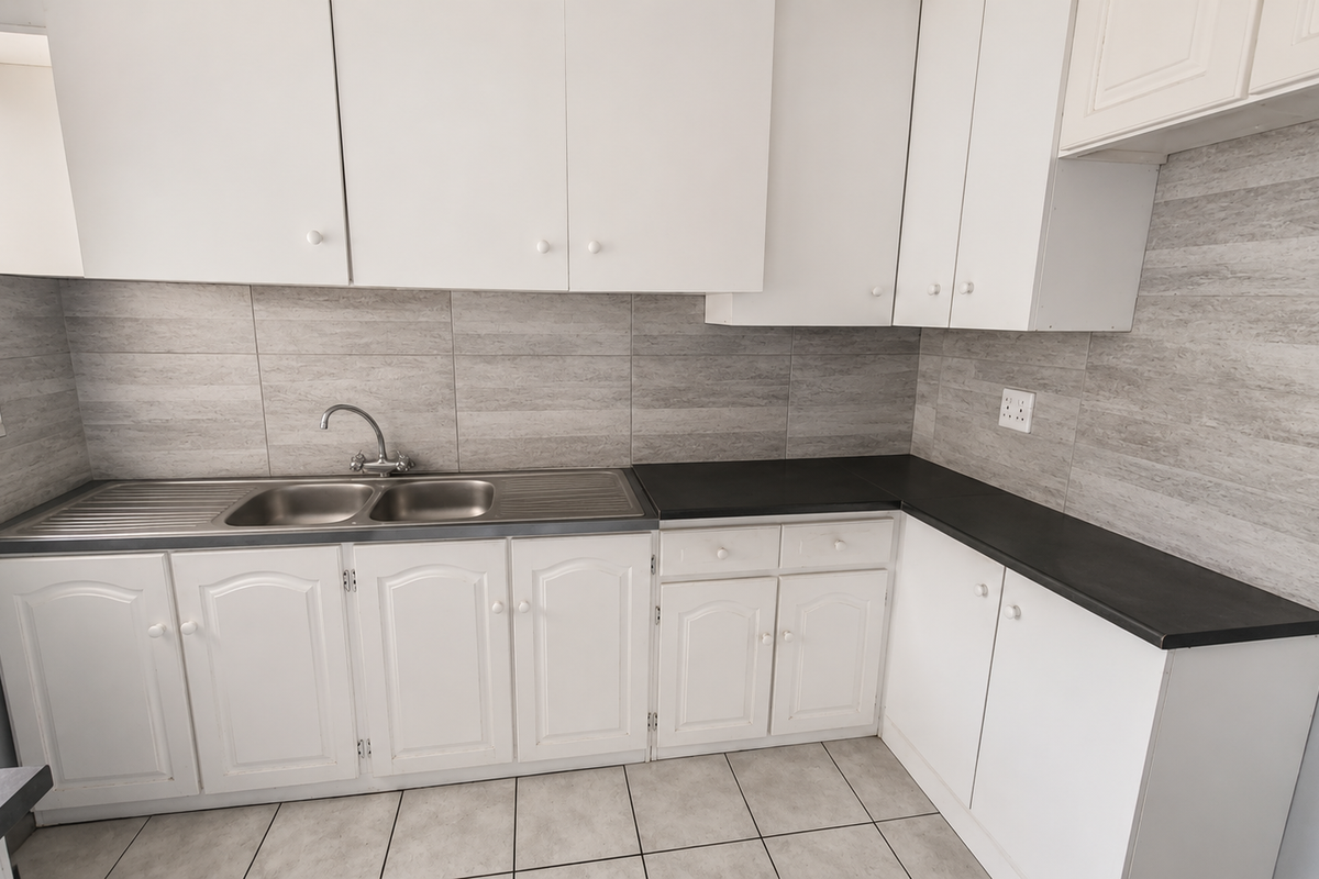 A clean, functional kitchen featuring white cabinetry, dark laminate countertops, a double stainless steel sink, and neutral tiled backsplash and flooring.