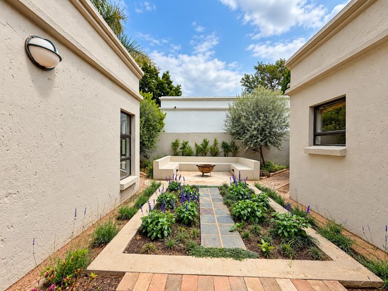 A beautifully landscaped courtyard featuring a central stone walkway, raised garden beds, and a built-in concrete bench, creating a serene outdoor seating area.