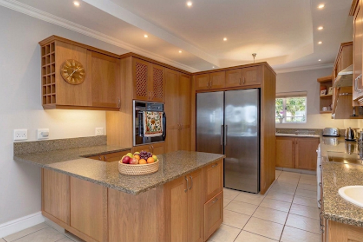 A well-maintained kitchen featuring wooden cabinetry, granite countertops, a built-in oven, and a double-door refrigerator, complemented by recessed ceiling lighting and tiled flooring.