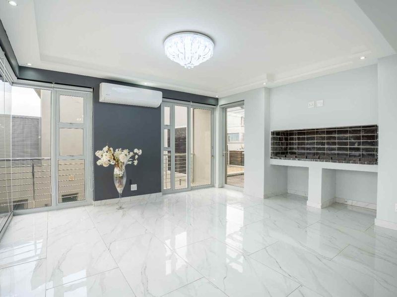 Modern open-plan living area featuring polished marble-look floor tiles, a built-in braai, air conditioning, and large sliding doors leading to an outdoor space.