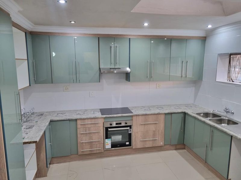 Modern kitchen featuring light green and wood-grain cabinetry, stone-look laminate countertops, integrated oven, electric hob, and a double bowl sink with tiled splashback.
