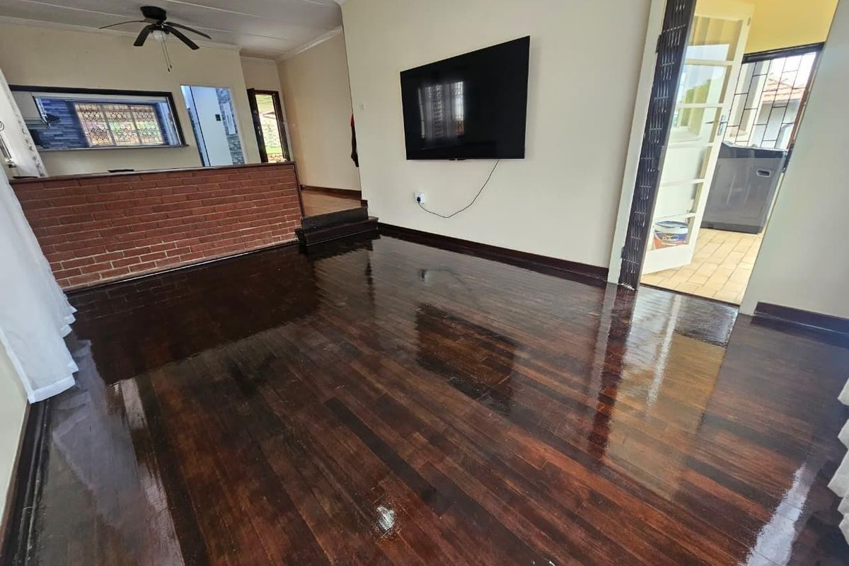 Spacious living area featuring polished timber flooring, a brick feature wall, and a ceiling fan, offering a clean and versatile space.