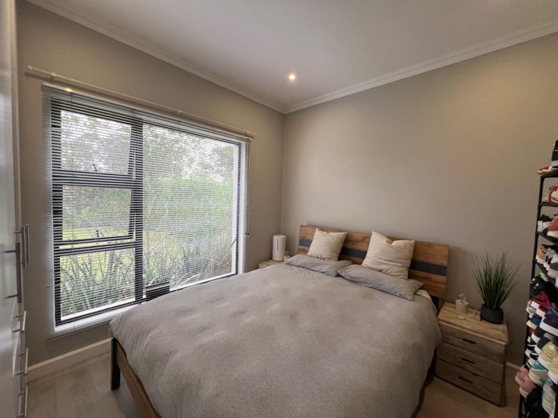 A well-maintained bedroom featuring neutral wall tones, laminate flooring, recessed lighting, and a large window with fitted venetian blinds overlooking the garden.