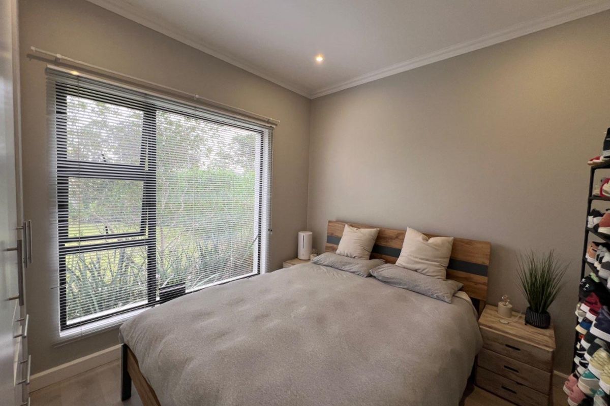 A well-maintained bedroom featuring neutral wall tones, laminate flooring, recessed lighting, and a large window with fitted venetian blinds overlooking the garden.