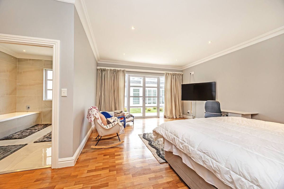 Spacious bedroom featuring hardwood flooring, crown molding, recessed lighting, and direct access to the garden through french doors, with an adjoining en-suite bathroom.