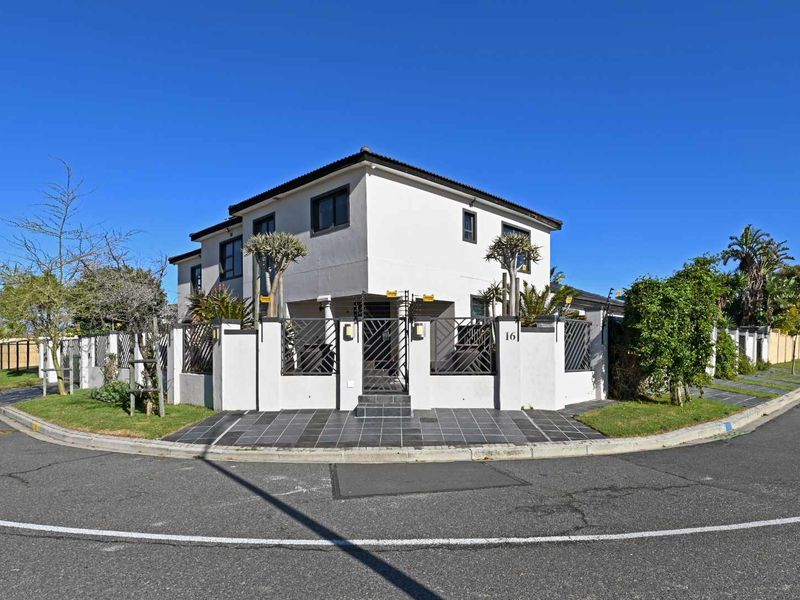 A corner-lot double-story house featuring a white facade, secure perimeter wall with electric fencing, and a tiled entrance path.