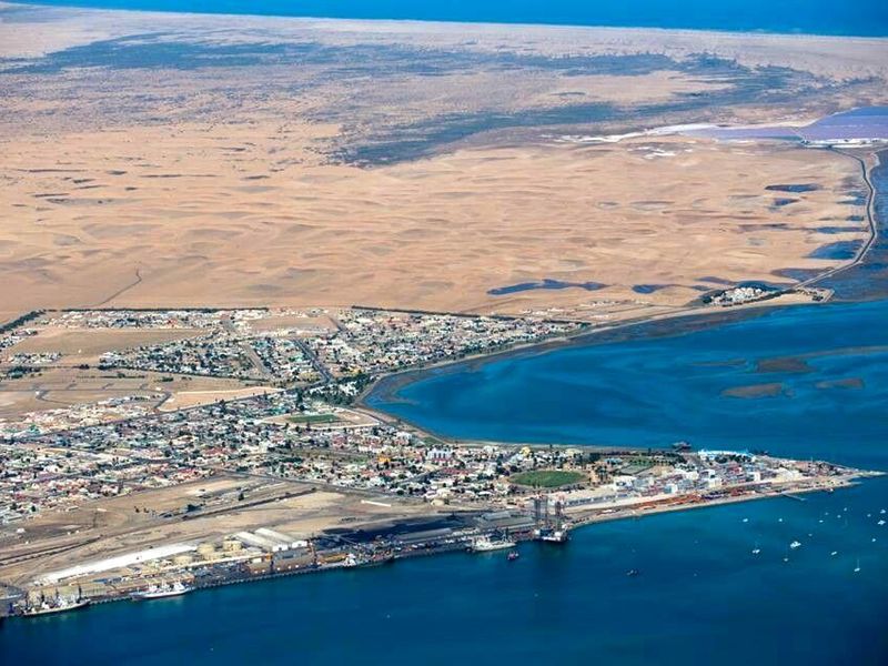 An aerial view of the coastal town and surrounding desert landscape, showcasing the proximity to the harbor and ocean.
