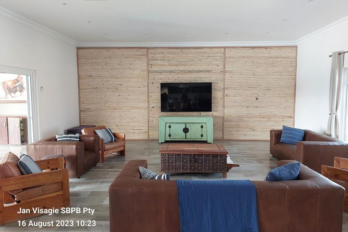 Spacious living room featuring a prominent timber-clad feature wall, recessed ceiling lighting, and large-format floor tiles.