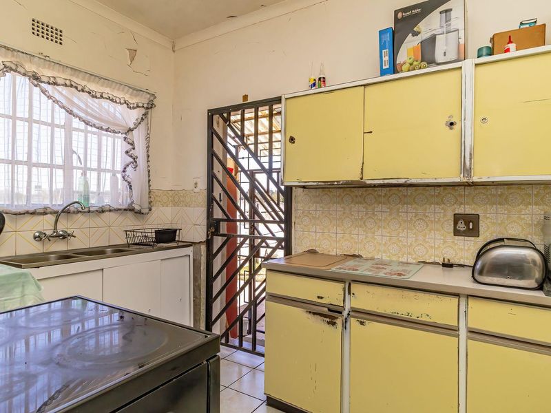 A dated kitchen featuring original yellow cabinetry, tiled backsplash, and a double sink, requiring significant renovation and cosmetic updates to modernize the space.