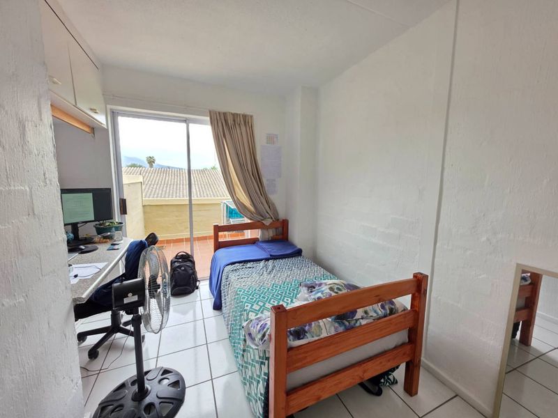 A functional bedroom featuring tiled flooring, a built-in desk with overhead storage, and a sliding glass door providing access to an outdoor balcony area.