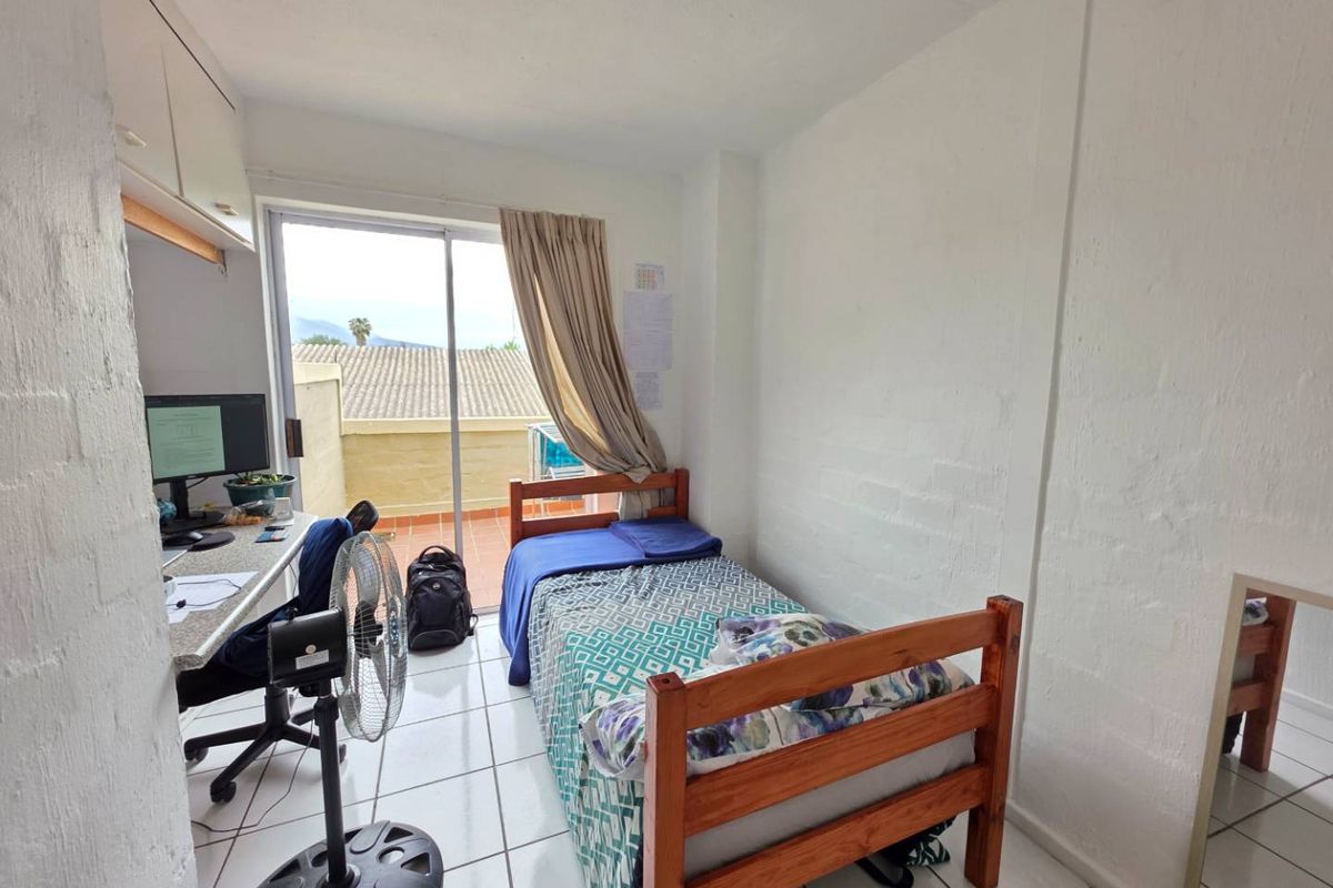 A functional bedroom featuring tiled flooring, a built-in desk with overhead storage, and a sliding glass door providing access to an outdoor balcony area.