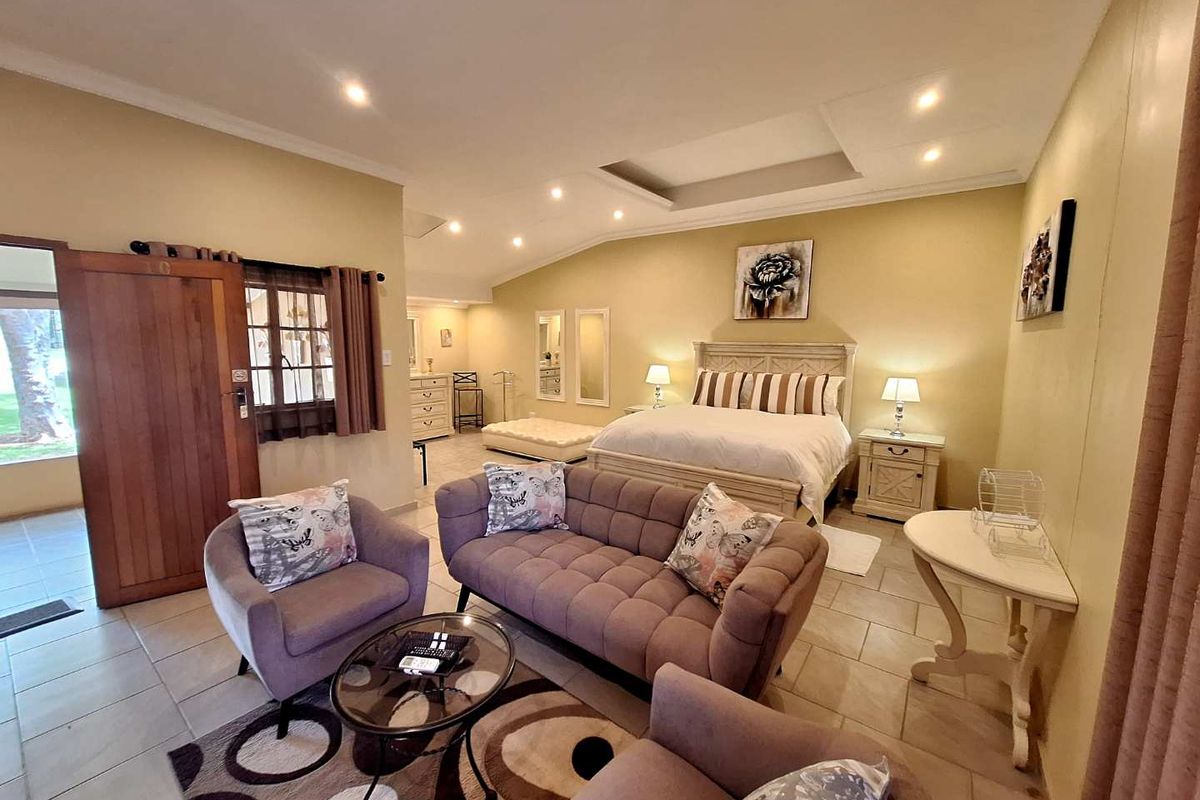 Spacious bedroom suite featuring a recessed ceiling with integrated downlighting, tiled flooring, and an open-plan layout with a comfortable seating area.