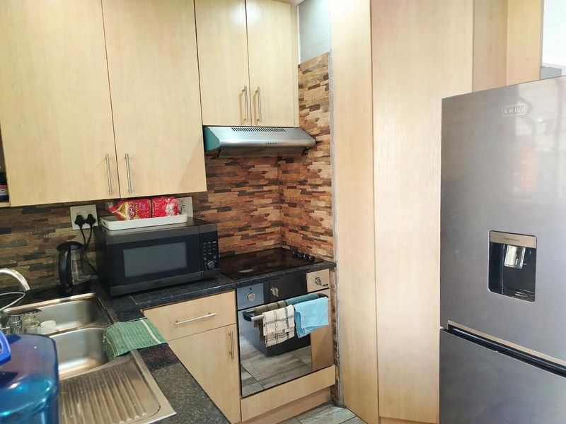 Compact kitchen featuring light wood cabinetry, granite countertops, a stone-look backsplash, and integrated appliances including an oven, hob, and extractor fan.