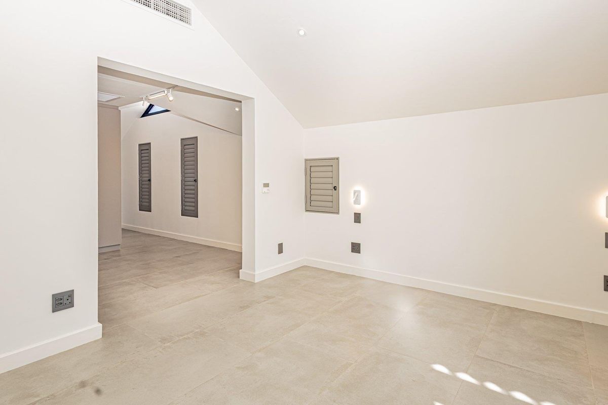 A bright, modern, and spacious living area featuring neutral tiled flooring, vaulted ceilings with recessed lighting, and clean, minimalist finishes throughout.