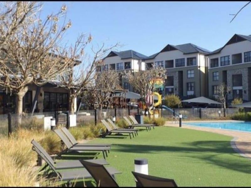 Communal pool area featuring a swimming pool, artificial lawn, and paved surrounds within a well-maintained apartment complex.