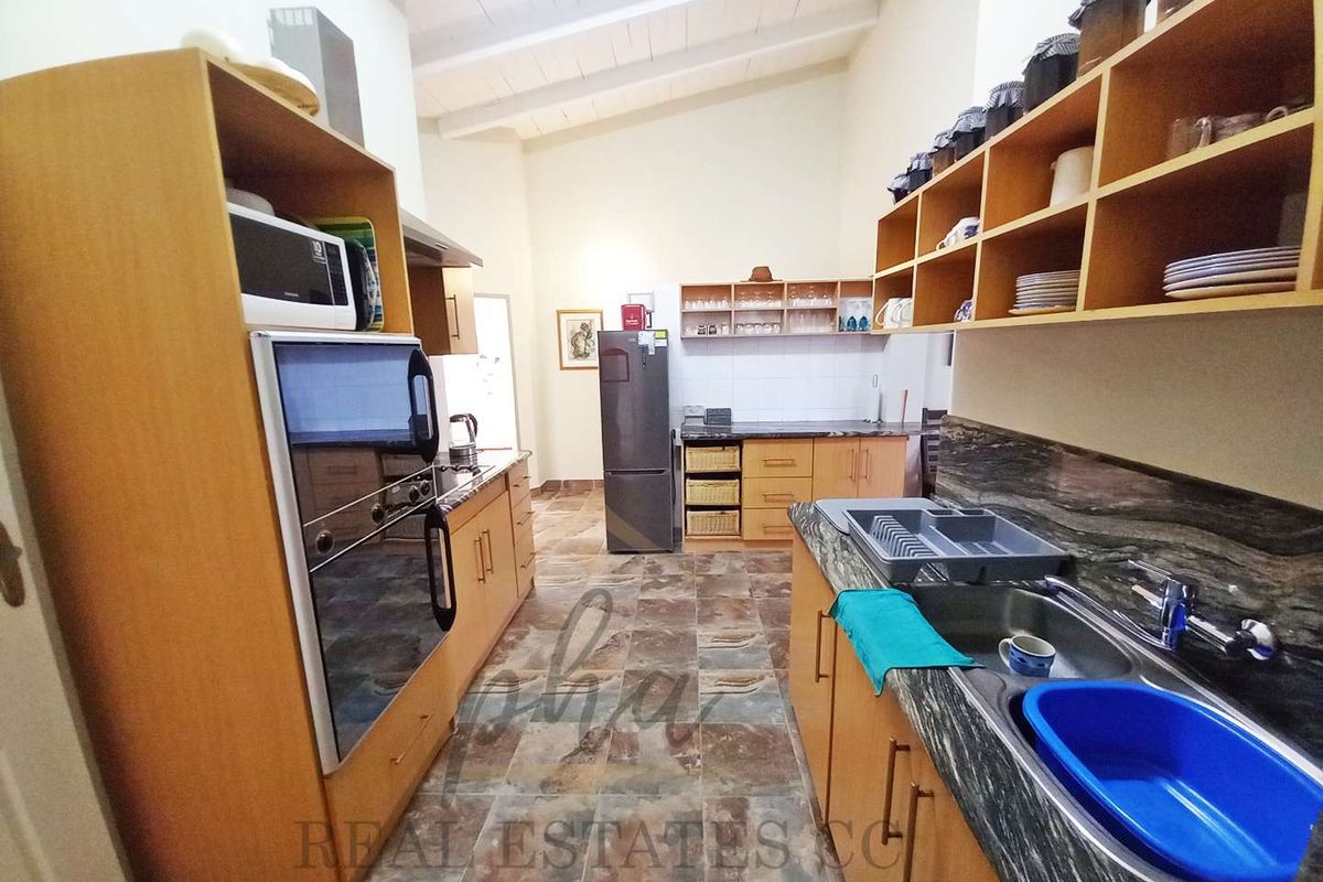 A functional kitchen featuring wooden cabinetry, stone-look countertops, a double sink, and a high vaulted ceiling with exposed beams.