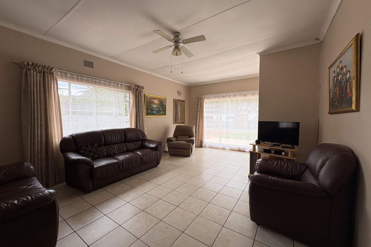 Spacious living room featuring large windows, tiled flooring, and a ceiling fan, offering a bright and functional area for relaxation.
