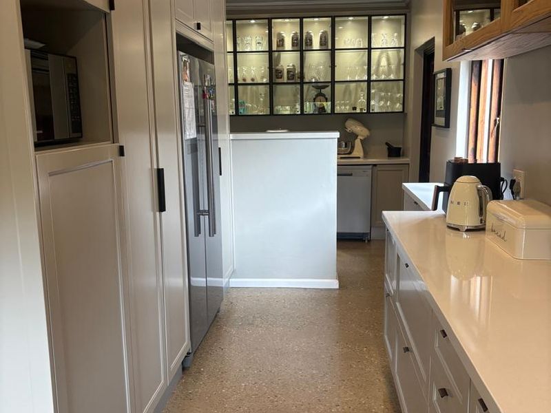 Modern kitchen featuring sleek cabinetry, quartz countertops, terrazzo flooring, and elegant glass-front display cabinets with integrated lighting.