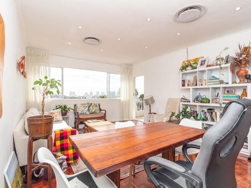 A bright living room featuring parquet flooring, recessed lighting, ducted air conditioning, and a large window with city views.