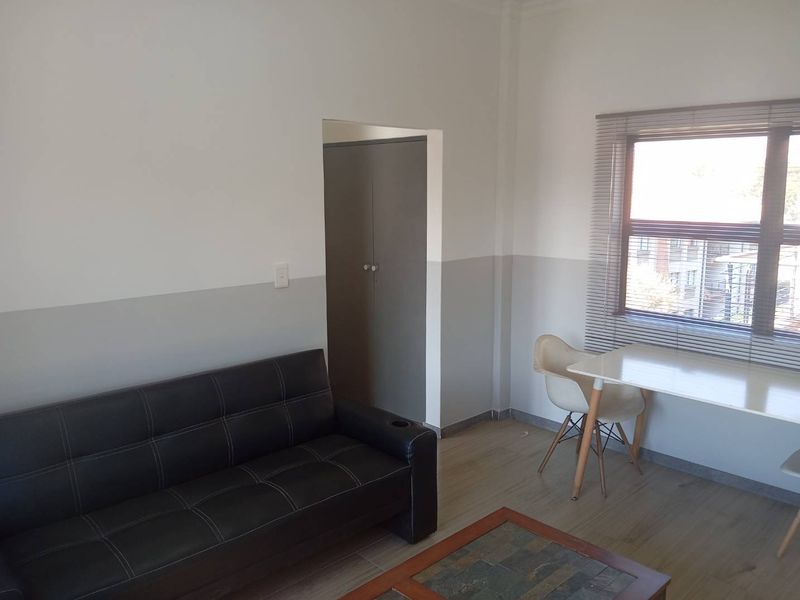 A living room featuring laminate flooring, a built-in cupboard, and a window fitted with venetian blinds.
