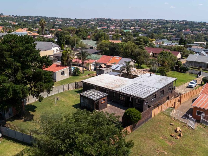 Aerial view of a residential property featuring a large garden, paved patio area, and a brick structure with a corrugated metal roof.