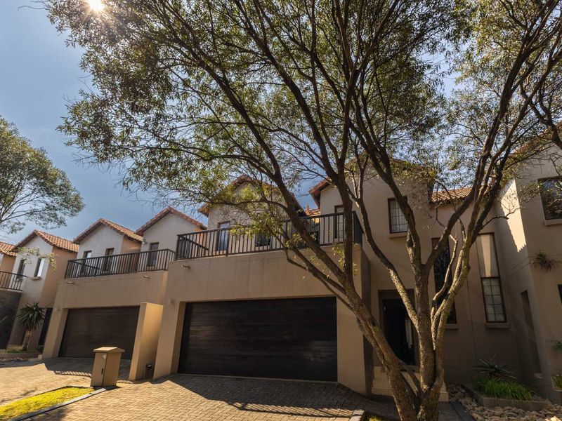 Front elevation of a townhouse featuring a paved driveway, double garage, and an upper-level balcony with metal railings.