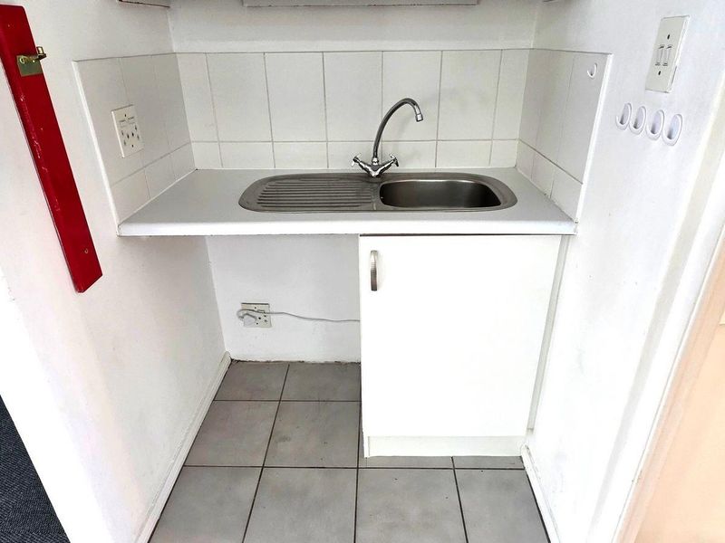 A compact kitchenette area featuring a stainless steel sink, tiled backsplash, and base cabinetry, suitable for office utility use.