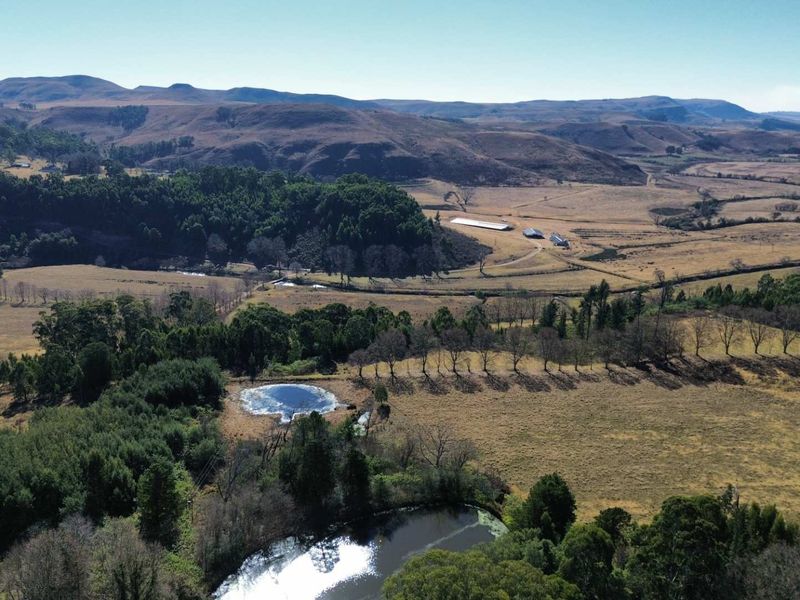 An expansive aerial view of the farm property, showcasing rolling hills, natural dams, established woodland, and distant outbuildings.