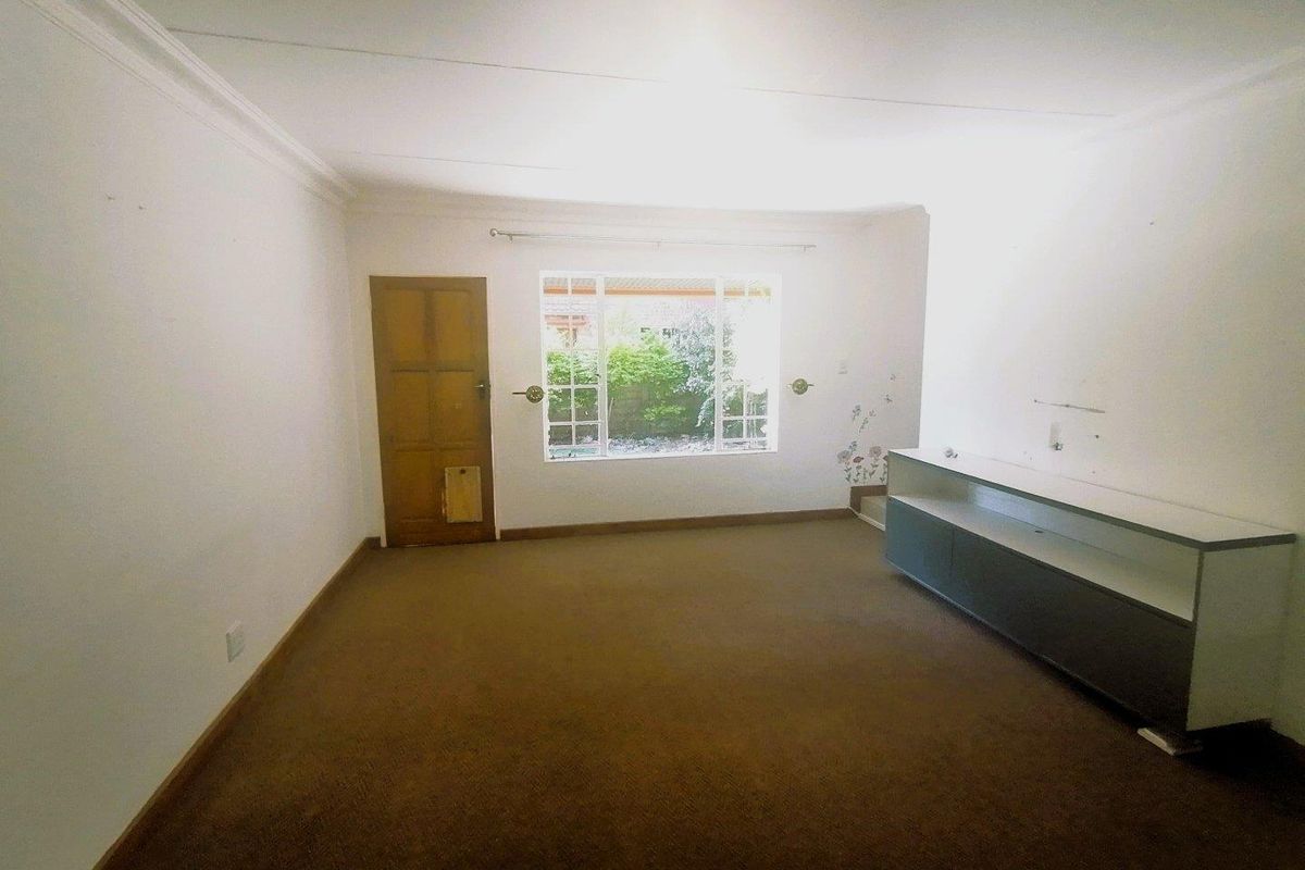 An empty living room featuring carpet flooring, built-in cabinetry, and a window with garden views, offering a blank canvas for renovation.