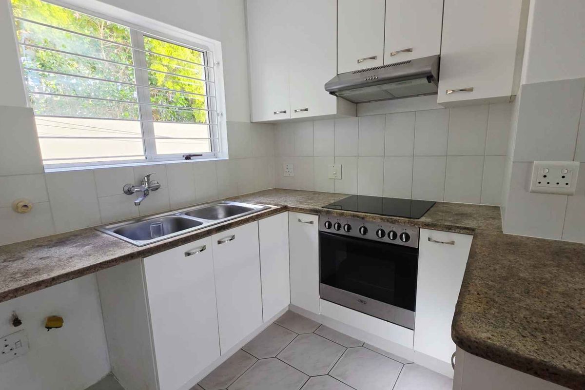 A functional kitchen featuring white cabinetry, stone-look countertops, a built-in oven, electric hob, extractor fan, and a double stainless steel sink.