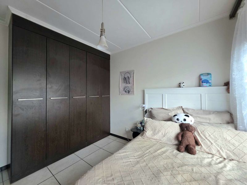 A well-maintained bedroom featuring dark wood built-in cupboards, neutral tiled flooring, and a simple pendant light fixture.