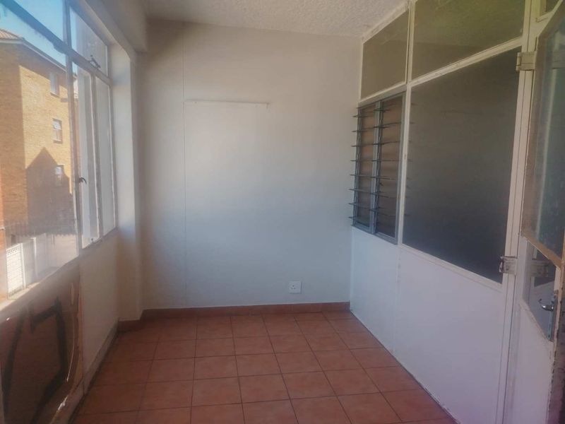 An enclosed balcony or sunroom featuring tiled flooring, large windows, and a glass partition wall, offering a versatile space for potential renovation.