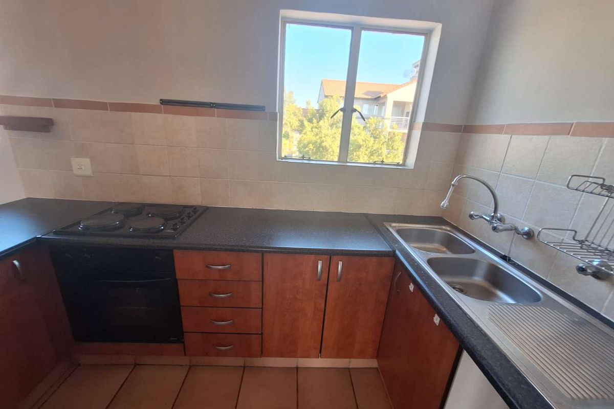 A functional kitchen featuring wooden cabinetry, dark laminate countertops, a built-in oven and hob, and a double bowl stainless steel sink with tiled backsplash.