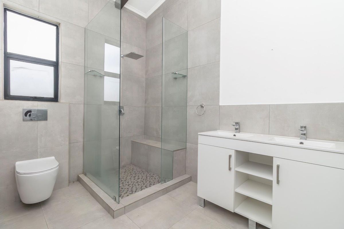 Modern bathroom featuring a walk-in glass shower with a built-in bench, a double vanity with storage, and a wall-mounted toilet.