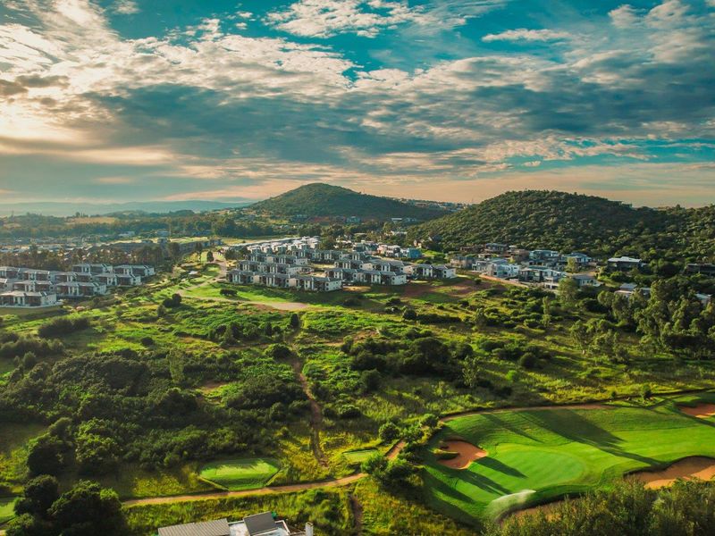 An aerial view of a residential estate integrated with a golf course, showcasing the surrounding landscape and hilly terrain.