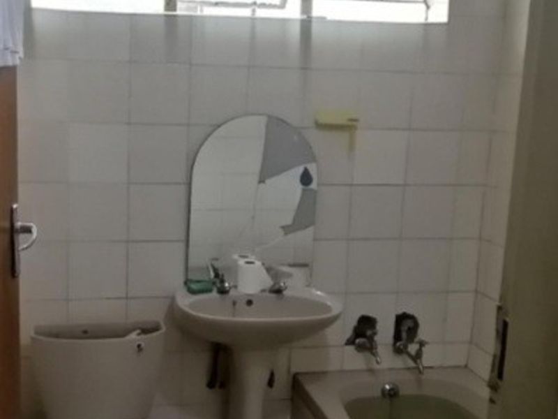 A dated bathroom featuring a pedestal basin, built-in bathtub, and toilet, requiring renovation to update the finishes and address visible wear.