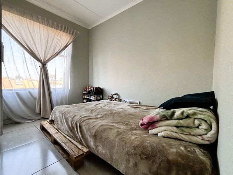 A bedroom featuring tiled flooring and a large window with curtain rails, providing natural light to the space.