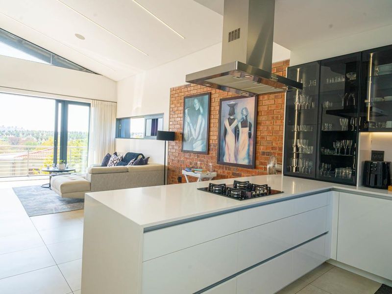 Modern open-plan living area featuring a sleek kitchen with gas hob, extractor fan, and exposed brick wall, flowing seamlessly to a balcony with views.