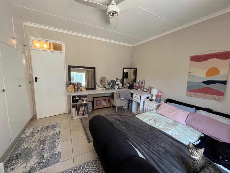 A bedroom featuring tiled flooring, built-in cupboards, and a ceiling fan, providing a functional and well-lit living space.