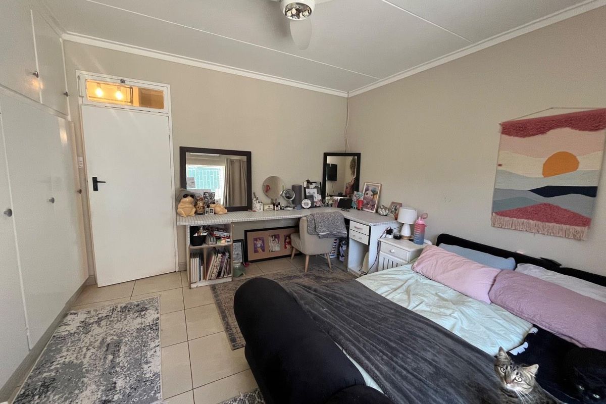A bedroom featuring tiled flooring, built-in cupboards, and a ceiling fan, providing a functional and well-lit living space.