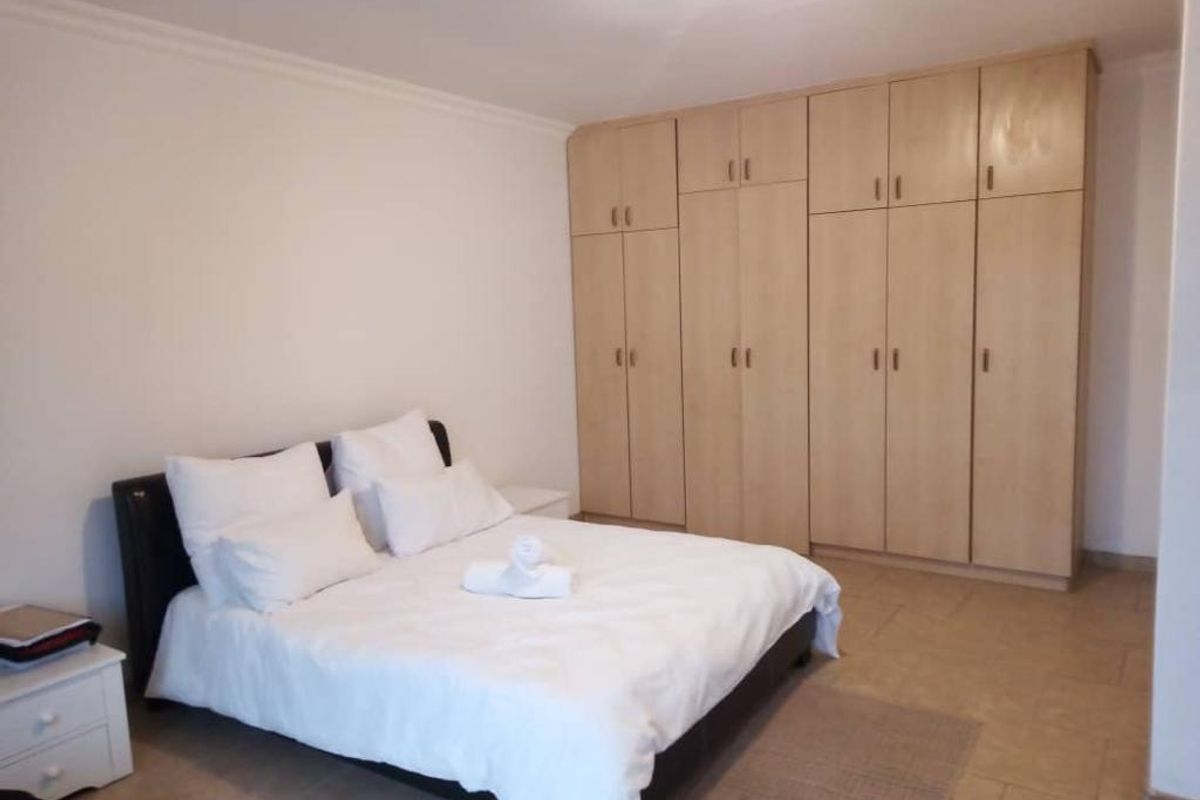 A spacious bedroom featuring extensive built-in wooden cabinetry providing ample storage and tiled flooring throughout.
