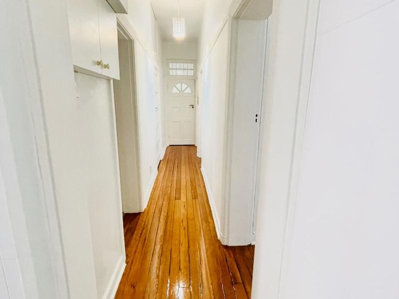 A bright, clean hallway featuring polished hardwood flooring, high ceilings, and built-in overhead storage cabinetry leading to a classic panelled entrance door.